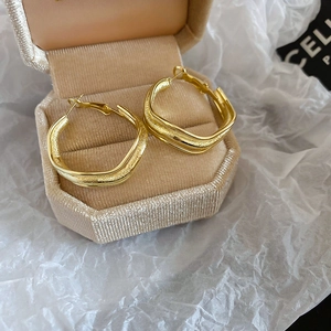 Detailed view of large irregular wavy gold hoop earrings in an octagonal jewelry box