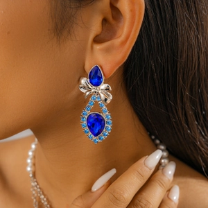 Close-up of teardrop blue gemstone earrings with silver bow detail worn by model