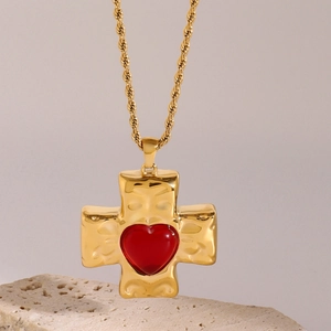 Macro shot of gold cross pendant with hammered texture and red heart gemstone inlay