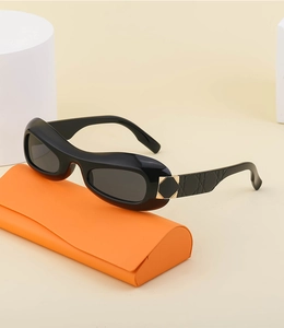 Detail of black oval Y2K sunglasses with orange folding case on warm beige studio background