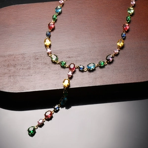 Macro shot of 18K gold chain necklace with colorful oval gemstones on dark reflective base