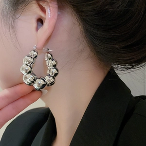 Close-up of silver U-shaped hoop earrings with textured bubble design on female model