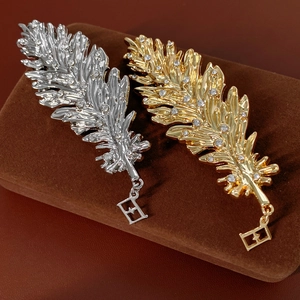 Detail view of gold and silver feather brooches with crystal inlay and E-letter charms