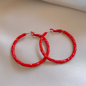 Close-up of red circular hoop earrings with unique hammered texture on beige fabric