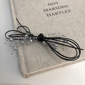 Detail of silver beaded chain and black cord bow hair clip on a minimalist linen book