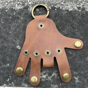 Nahaufnahme brauner Leder-Schlüsselanhänger in Handform mit Messingknöpfen auf Beton