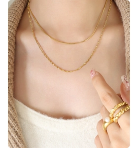 Detail of layered gold snake chain necklace and pearl ring on female model