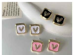 Dettaglio di orecchini a cuore quadrati in smalto nero, bianco e rosa con finitura oro