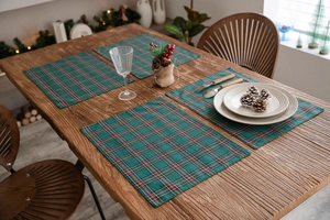 Set of four green plaid Christmas placemats on a wooden table with festive decor