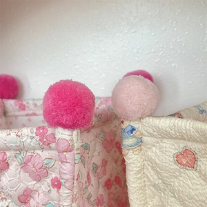 Detailed close-up of quilted storage baskets with colorful pom-pom edges and floral patterns