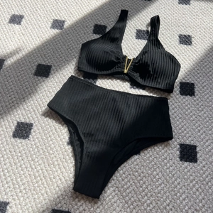 Solid black ribbed high-waisted bikini set with golden V-metal detail on flat lay surface