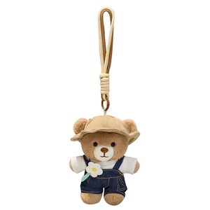 Cute brown plush teddy bear keychain in denim overalls with floral detail and woven lanyard