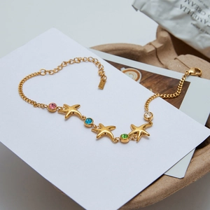 Detailed shot of golden starfish bracelet with pink, blue, and green zircons on white card