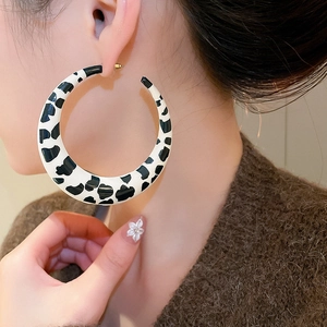Close-up of large C-shaped cow print earrings worn with a minimalist fashion style