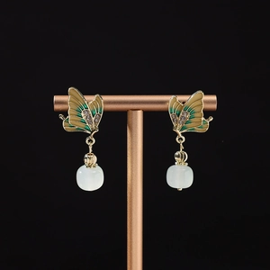 Detailed macro of golden butterfly earrings with enamel wings and white jade pendant