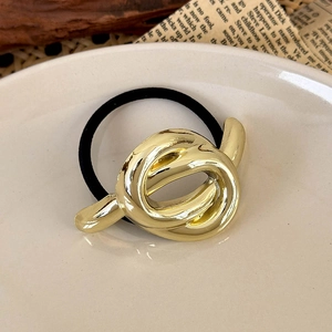 Detail of a minimalist golden twisted metal charm on high-elastic black hair tie