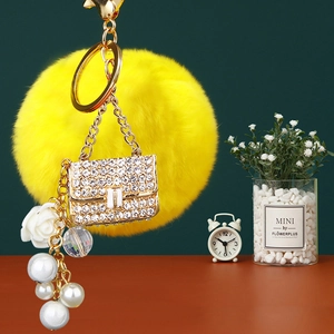Detail view of yellow faux fur pompom keychain with rhinestone handbag and pearls