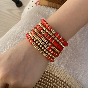 Bohemian style multi-layer red and gold beaded clay disc bracelets worn on wrist