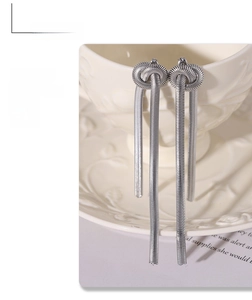 Detail of silver knot snake chain tassel earrings hanging on a ceramic cup edge
