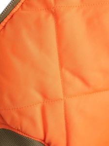 Macro shot of bright orange quilted lining with olive green zipper and ribbed cuff detail