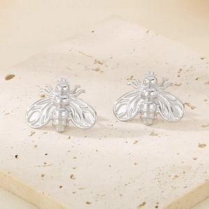 Detailed close-up of two silver-colored bee-shaped earrings on a beige stone base