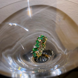 Vue détaillée bague dorée avec zircon vert rectangulaire dans un verre à cocktail