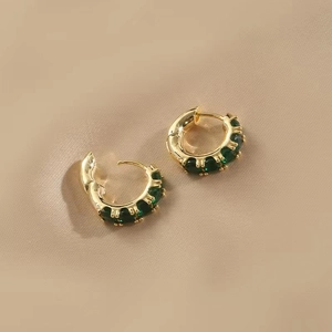Elegant gold C-shaped hoop earrings with green zircon stones on soft beige fabric
