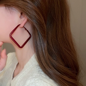 Macro shot of large burgundy diamond shaped lacquer earrings on model with white top