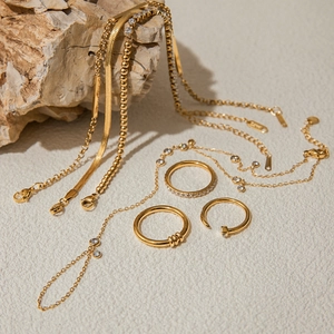 Gold stainless steel jewelry set with layered bracelets and rings on a natural stone