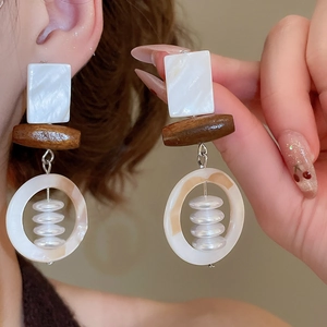 Detail of geometric earrings featuring square shell and wood texture with beads