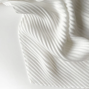 Detailed close-up of white pleated fabric with accordion texture on cotton-linen scarf