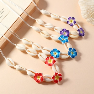 Trois colliers de fleurs en coquillage en violet, bleu et rouge sur fond neutre chaud