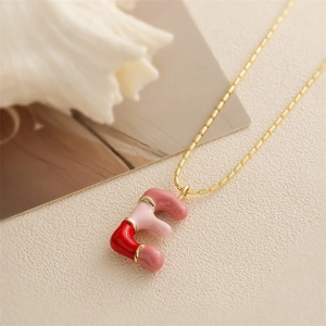 Détail du collier chaîne dorée avec pendentif lettre F en émail rouge et rose