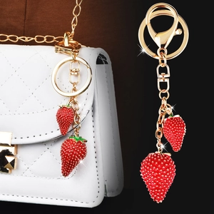 Llavero de fresa roja elegante en bolso blanco y sobre un fondo negro