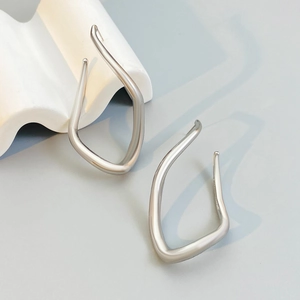 Detail of silver geometric hoop earrings on white plaster stand with a smooth metallic finish