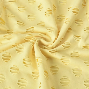 Detailed close-up of pale yellow knitted fabric with circular laser-cut hollow out design