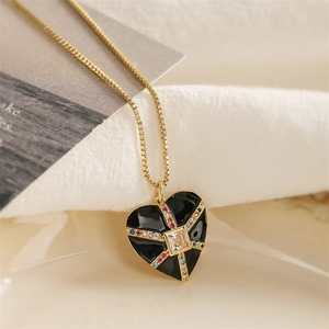 Détail d'un pendentif cœur doré avec émail noir et gemmes colorées sur tissu blanc
