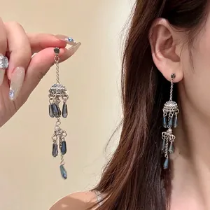 Detailed view of silver long fringe earrings with blue teardrop crystals worn by model