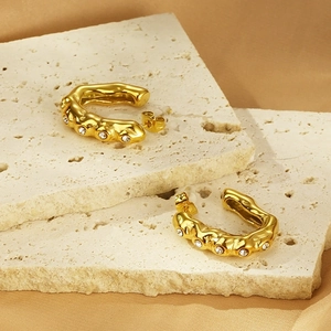 Détail de boucles d'oreilles en U dorées martelées avec cristaux blancs sur travertin
