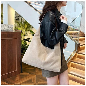 Side view of beige suede tote bag worn by model in a modern indoor staircase setting