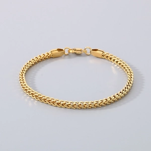 Dettaglio di un bracciale a maglia spiga dorata con chiusura a moschettone su grigio