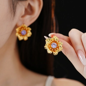 Close-up of gold flower earrings with purple zircon stone on a model with black background