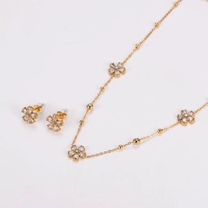 Close-up of golden stainless steel necklace and stud earrings set with crystal flower motif