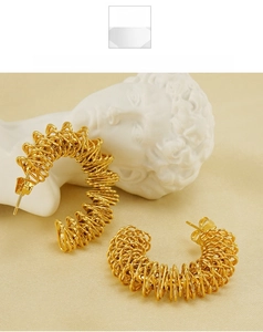 Close-up of golden spiral C-shaped earrings with woven texture on beige silk