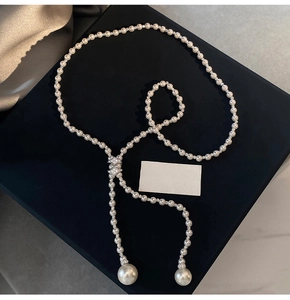 Detailed view of elegant Y-shaped pearl necklace with zircon accents on black velvet background
