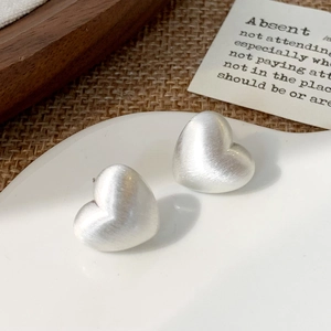 Macro di orecchini a cuore in argento spazzolato su un vassoio di ceramica bianca