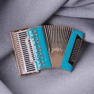 Detail of accordion enamel brooch with blue, white and black details on grey fabric