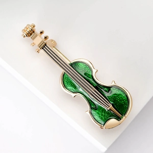 Macro shot of gold violin brooch with green enamel details on white background