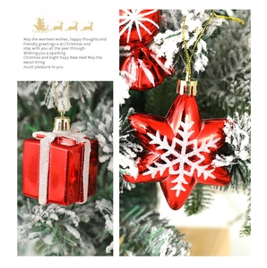 Detail of red gift box and snowflake star ornaments hanging on snowy Christmas tree branches