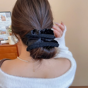 Macro shot of large black velvet hair scrunchie styled on a classic bun updo